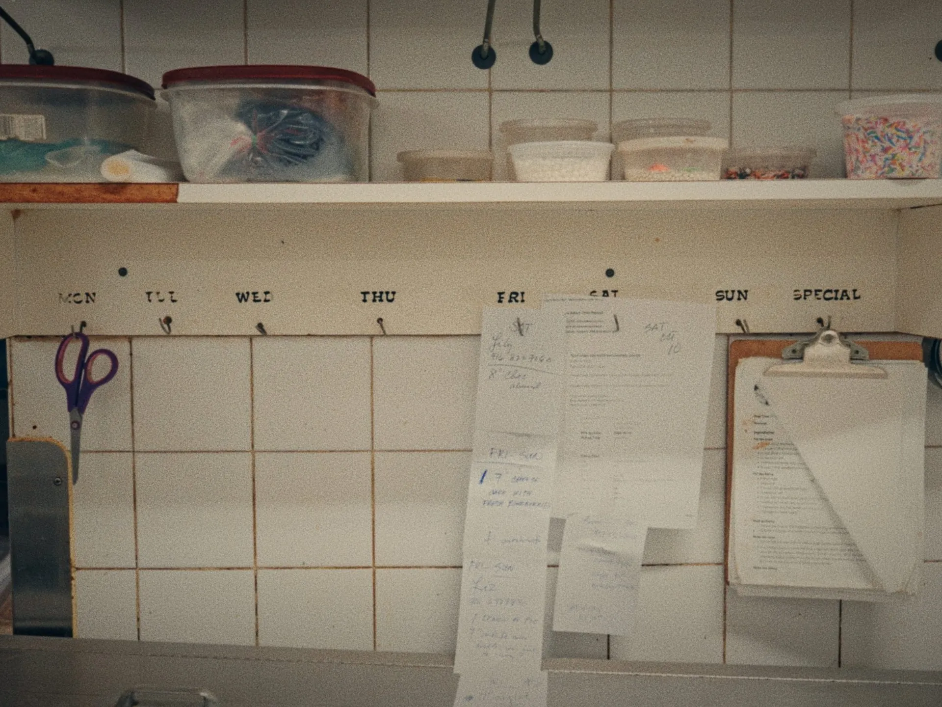 Orders for the week clipped under the days on a bakery wall, from Before Thanksgiving by Studio Propel