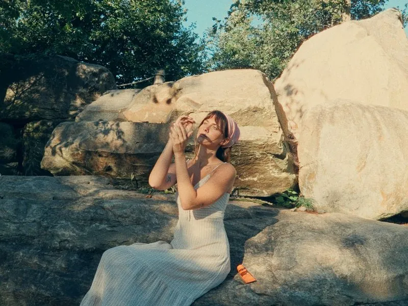 Sitting on sunlit rocks in a linen dress, from Thank You, Summer, an Aesop concept film by Studio Propel