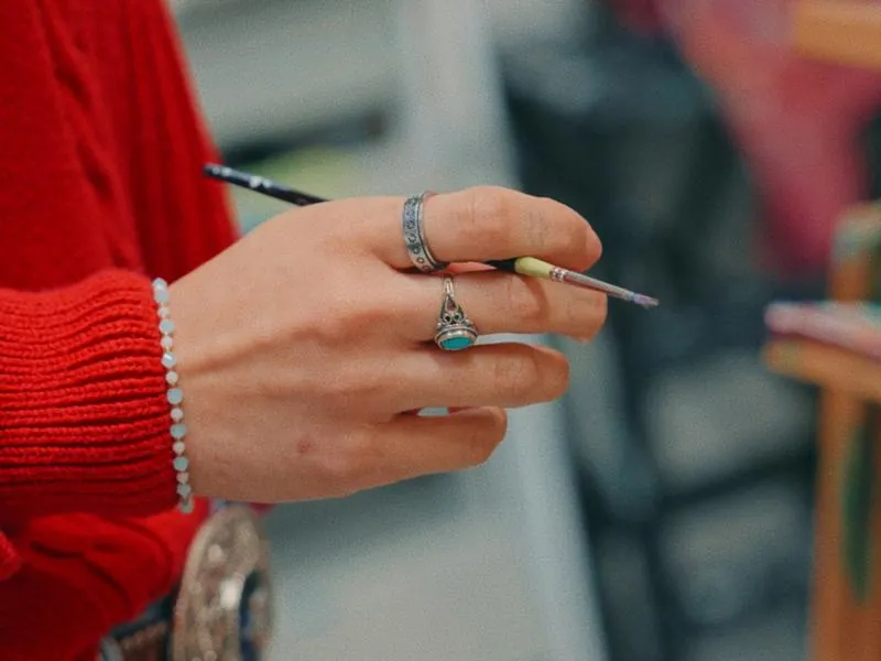 A paintbrush between ringed fingers, from Imposter Syndrome by Studio Propel